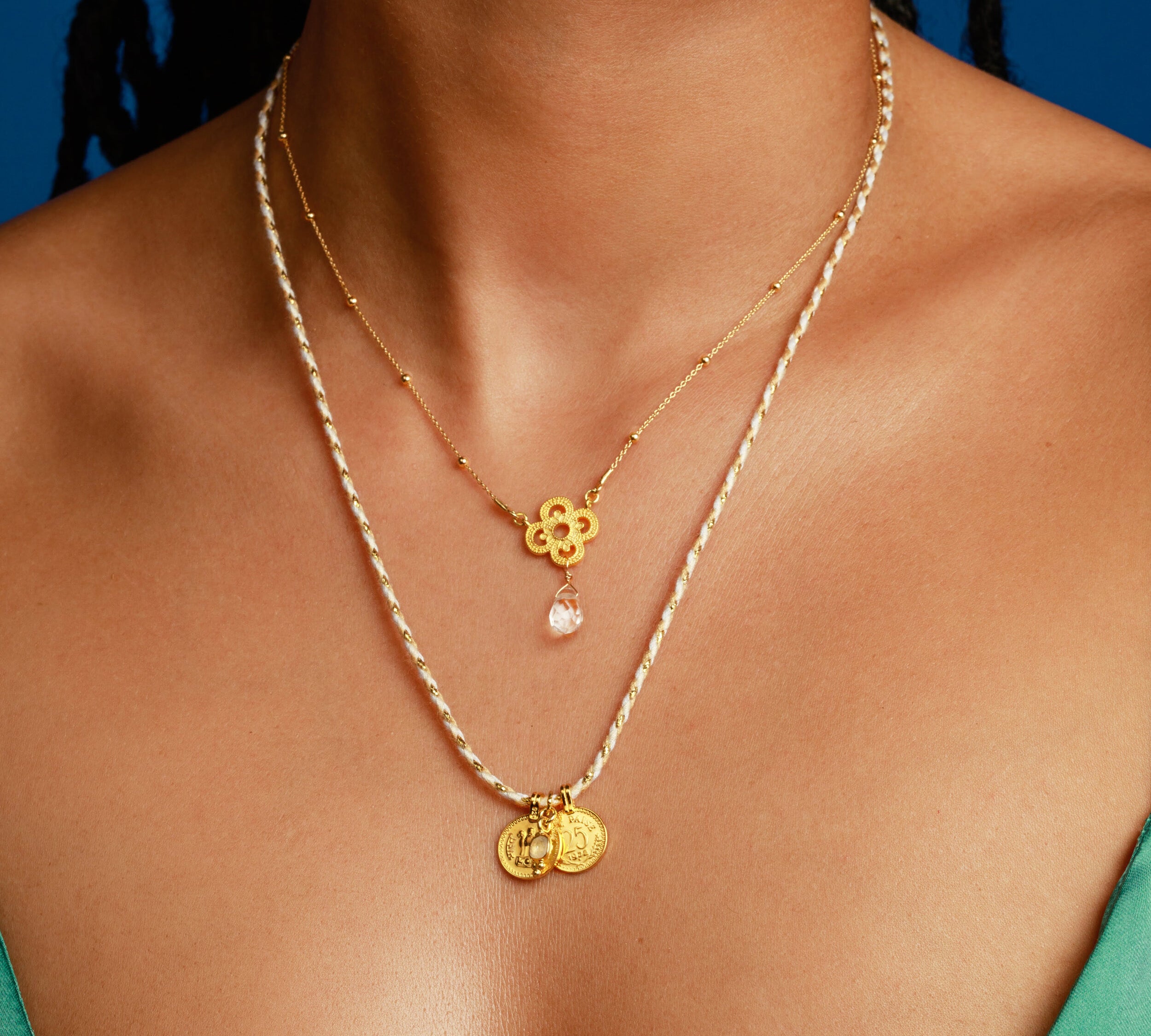 Dekolleté von Frau mit Kleeblatt Kette und Münz-Kette in Gold und Beige Tönen.