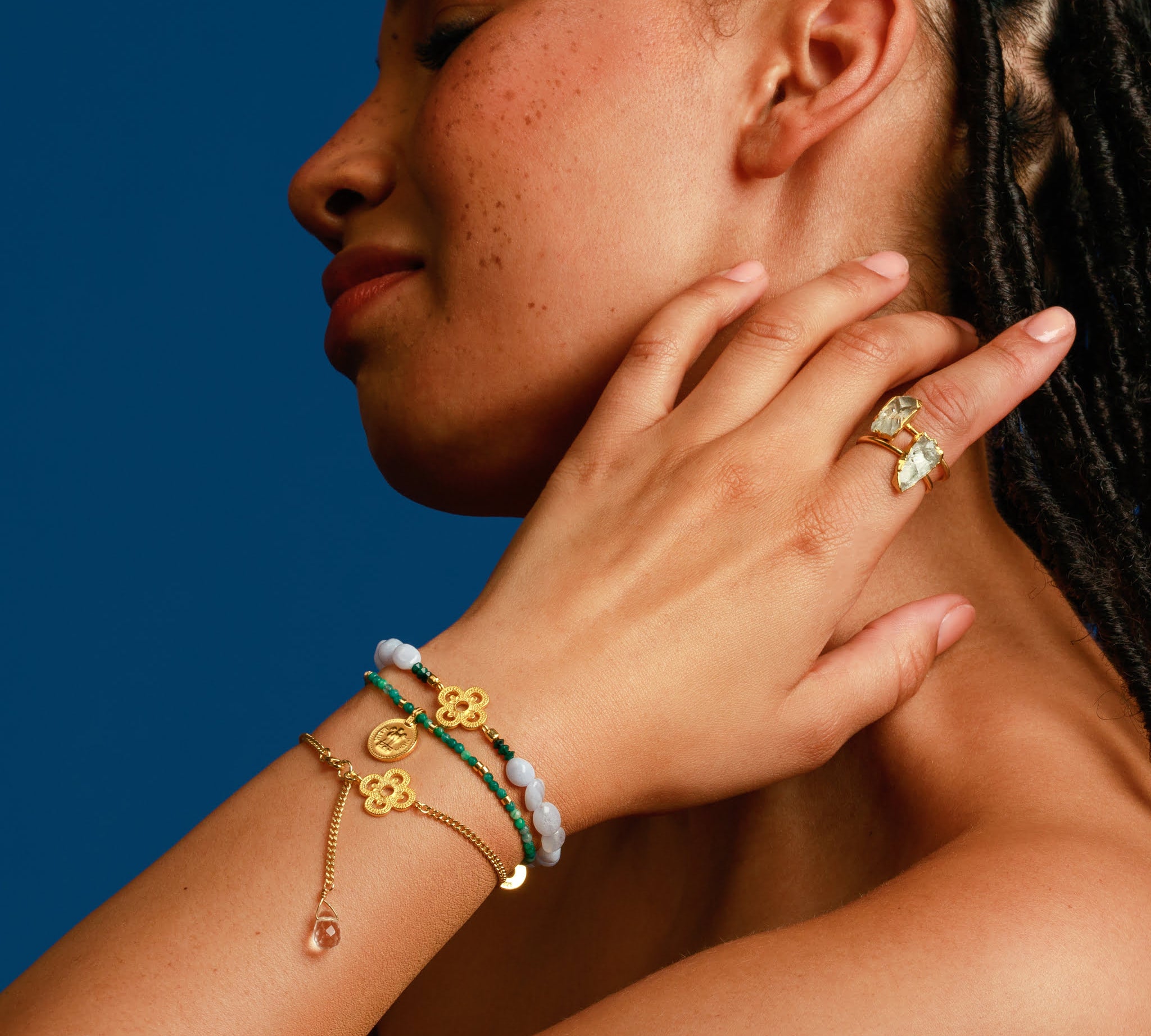 Frau trägt drei Armbänder mit Kleeblatt Motiven und einen Edelstein Ring.
